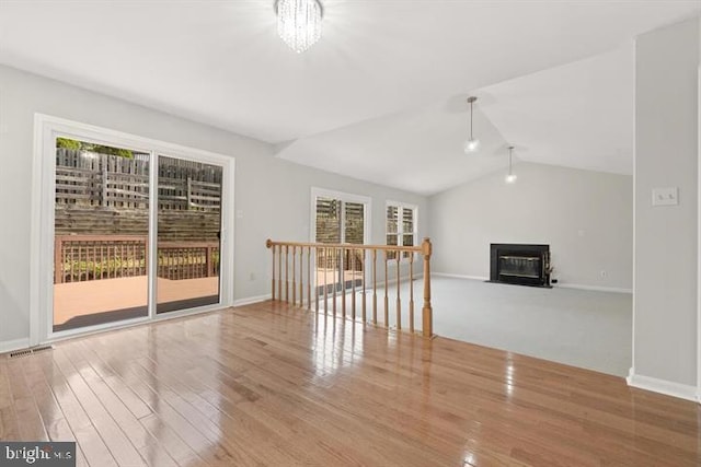 13017 Broadmore, Silver Spring, MD 20904 - unfurnished living room with healthy amount of natural light, a glass covered fireplace, wood finished floors, baseboards, and vaulted ceiling