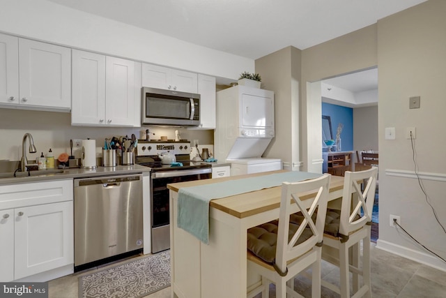 3713 S George Mason Dr Unit 713, Falls Church, VA 22041 - kitchen with appliances with stainless steel finishes, stacked washing machine and dryer, a sink, white cabinetry, and baseboards