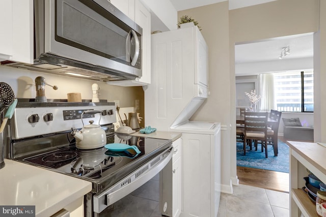 3713 S George Mason Dr Unit 713, Falls Church, VA 22041 - kitchen with stainless steel appliances, stacked washer / dryer, light tile patterned flooring, white cabinets, and light countertops