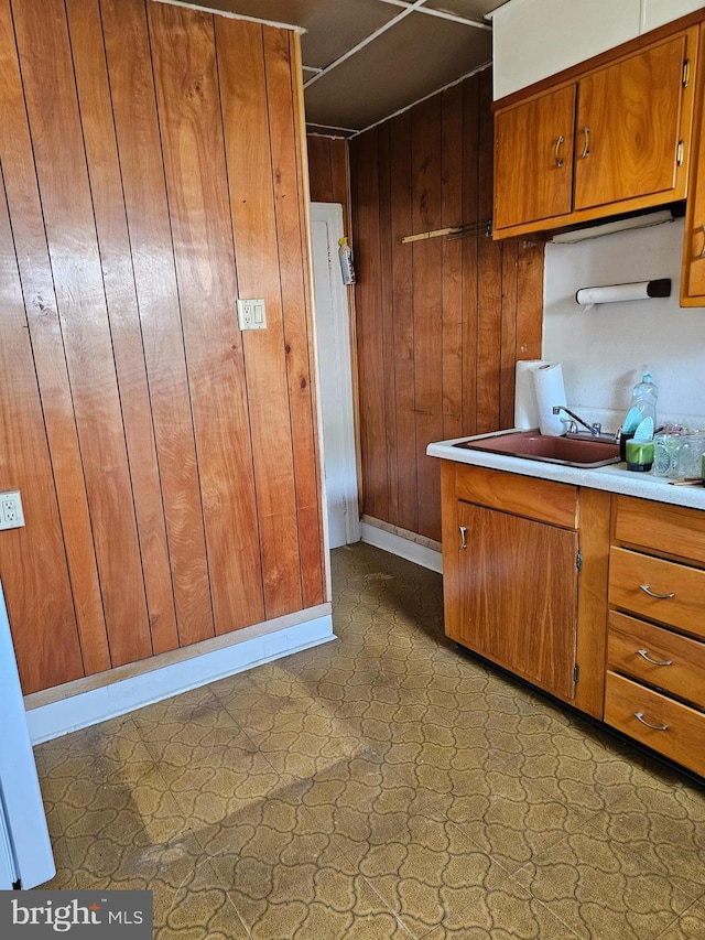 1943 W Sparks St, Philadelphia, PA 19141 - kitchen with brown cabinetry, wood walls, a sink, light countertops, and baseboards