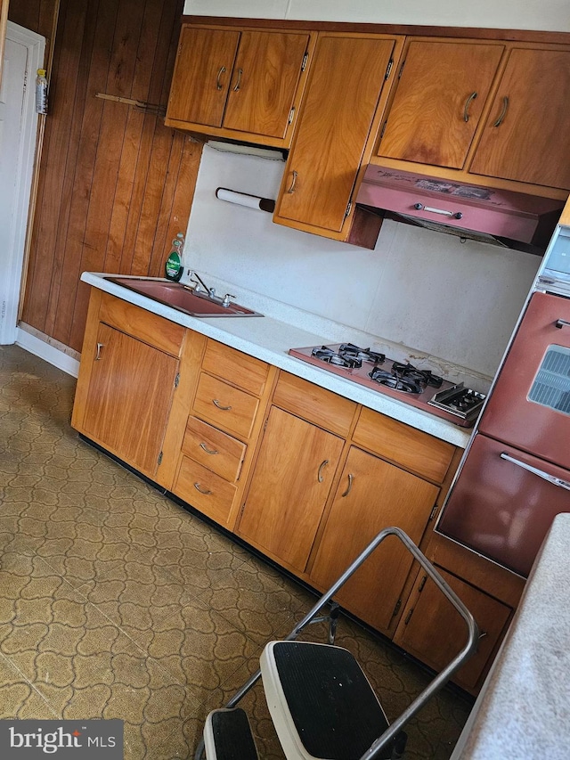 1943 W Sparks St, Philadelphia, PA 19141 - kitchen featuring brown cabinetry, light countertops, stainless steel gas cooktop, a sink, and wooden walls