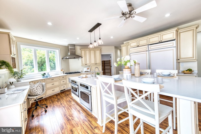 6153 Long Point Rd, Neavitt, MD 21652 - kitchen featuring cream cabinetry, wall chimney range hood, stainless steel oven, light countertops, and a breakfast bar area