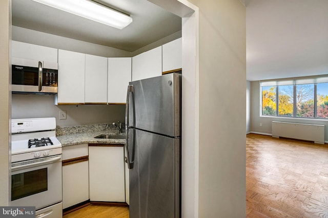 2939 Van Ness St NW Unit 1144, Washington, DC 20008 - kitchen featuring stainless steel appliances, a sink, radiator, white cabinetry, and light stone countertops