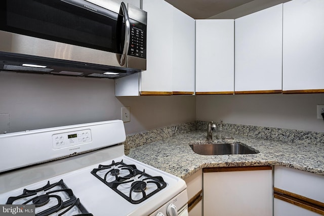 2939 Van Ness St NW Unit 1144, Washington, DC 20008 - kitchen with white gas range, stainless steel microwave, a sink, white cabinets, and light stone countertops