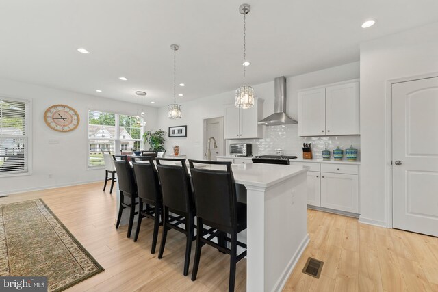 9400 Kinnerton Dr, Midlothian, VA 23112 - kitchen with wall chimney exhaust hood, light countertops, a kitchen island with sink, light wood finished floors, and stainless steel stove