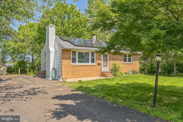 64 Poplar Ave, Warrington, PA 18976 - view of front of house featuring brick siding, a chimney, roof mounted solar panels, a front lawn, and driveway