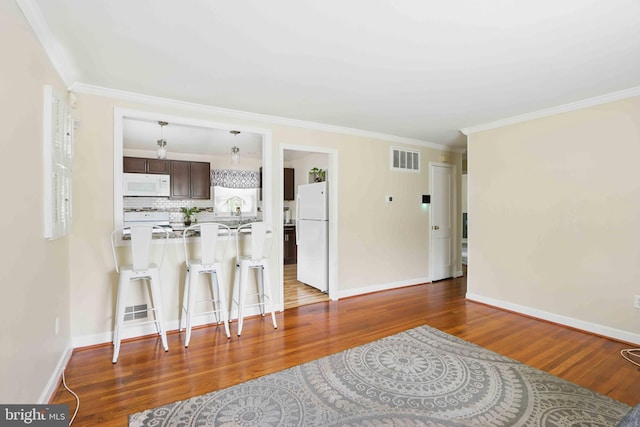 6937 Halleck St, District Heights, MD 20747 - kitchen featuring white appliances, a kitchen breakfast bar, dark brown cabinetry, wood finished floors, and crown molding