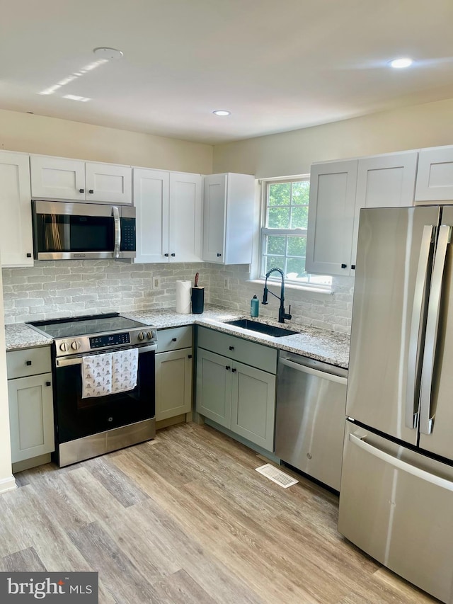 25795 Shamrock Ln, Mechanicsville, MD 20659 - kitchen with appliances with stainless steel finishes, a sink, light wood-type flooring, tasteful backsplash, and light stone countertops