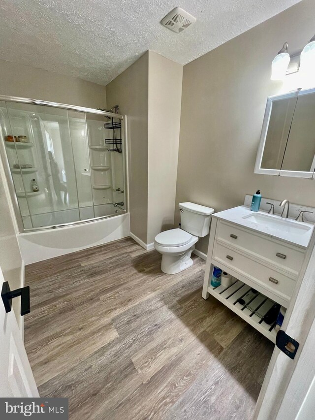 25795 Shamrock Ln, Mechanicsville, MD 20659 - bathroom featuring toilet, wood finished floors, a textured ceiling, vanity, and shower / bath combination with glass door