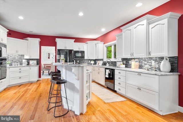 10840 Wolfsville Rd, Myersville, MD 21773 - kitchen featuring black appliances, a breakfast bar area, white cabinets, decorative backsplash, and light wood-style floors