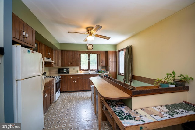 10496 Red Hawk Ln, Huntingdon, PA 16652 - kitchen with white appliances, under cabinet range hood, brown cabinetry, ceiling fan, and light floors