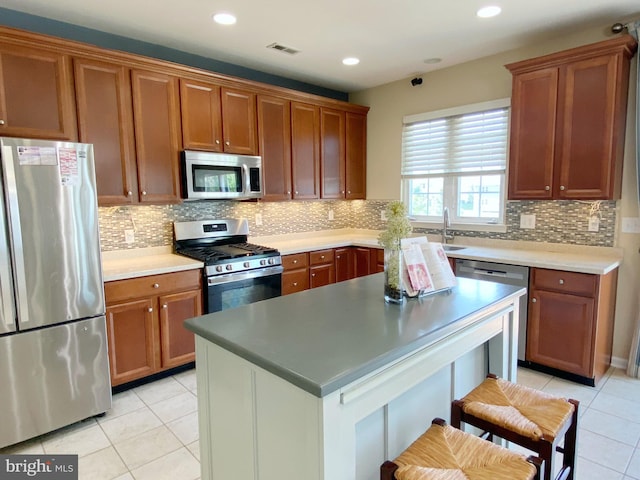 614 Empire Dr, Downingtown, PA 19335 - kitchen featuring stainless steel appliances, light tile patterned flooring, brown cabinets, backsplash, and a breakfast bar