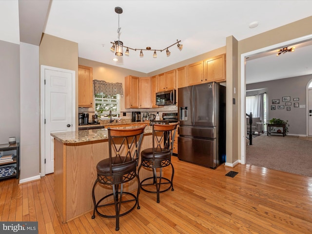 6529 Carston Ct, Frederick, MD 21703 - kitchen featuring appliances with stainless steel finishes, light brown cabinetry, a kitchen island, light wood finished floors, and a breakfast bar area