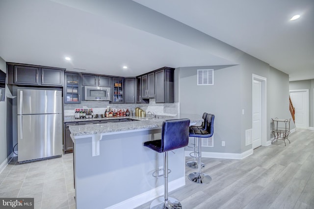 41031 Brook Grove Dr, Aldie, VA 20105 - kitchen featuring appliances with stainless steel finishes, a breakfast bar, glass insert cabinets, tasteful backsplash, and light stone countertops