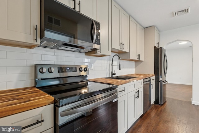 1631 Old Schuylkill Rd, Spring City, PA 19475 - kitchen featuring appliances with stainless steel finishes, butcher block countertops, arched walkways, dark wood finished floors, and decorative backsplash