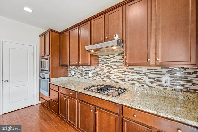41835 Diabase Sq, Aldie, VA 20105 - kitchen featuring stainless steel appliances, under cabinet range hood, light stone countertops, light wood finished floors, and brown cabinets