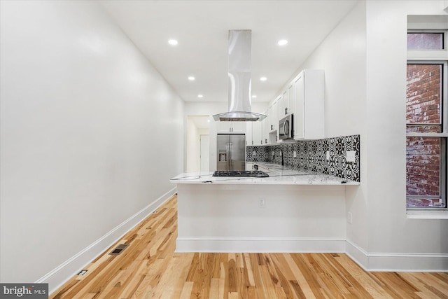 1630 E Biddle St, Baltimore, MD 21213 - kitchen featuring stainless steel appliances, island exhaust hood, white cabinetry, decorative backsplash, and light wood-type flooring