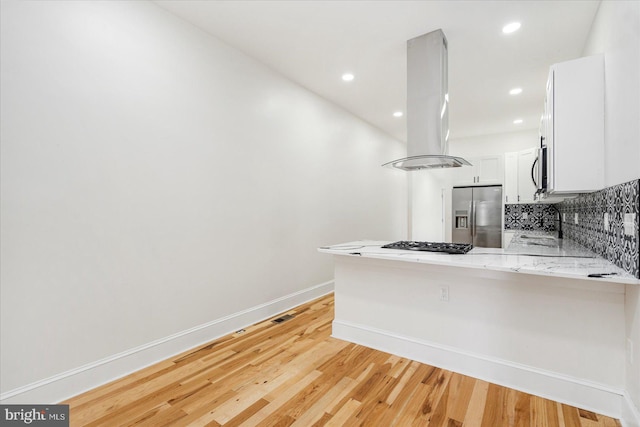 1630 E Biddle St, Baltimore, MD 21213 - kitchen featuring appliances with stainless steel finishes, island range hood, a peninsula, light wood-style floors, and tasteful backsplash