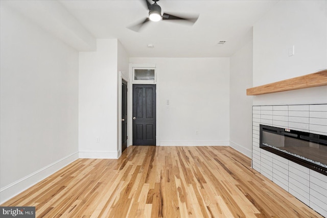 1630 E Biddle St, Baltimore, MD 21213 - unfurnished living room featuring light wood-type flooring, ceiling fan, a tiled fireplace, and baseboards