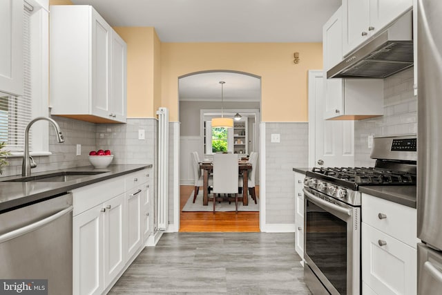 303 Conway Ave, Narberth, PA 19072 - kitchen featuring appliances with stainless steel finishes, under cabinet range hood, a sink, dark countertops, and arched walkways