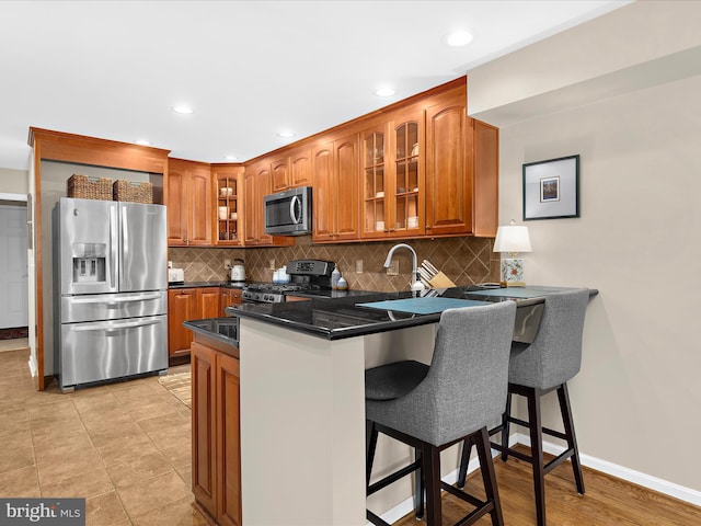 2772 Gingerview Ln, Annapolis, MD 21401 - kitchen featuring appliances with stainless steel finishes, a peninsula, brown cabinetry, glass insert cabinets, and decorative backsplash