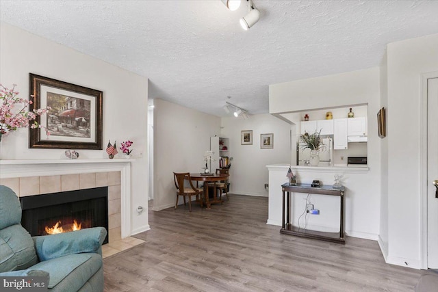 20273 Beechwood Ter Unit 103, Ashburn, VA 20147 - living room featuring rail lighting, light wood-type flooring, a textured ceiling, a tiled fireplace, and baseboards