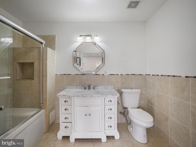 1705 E Chase St, Baltimore, MD 21213 - bathroom with tile patterned floors, toilet, vanity, tile walls, and shower / bath combination with glass door