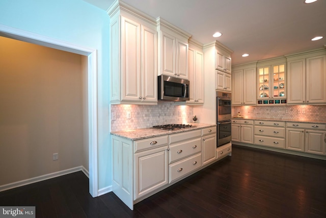 29486 Andrew Jackson Dr, Millsboro, DE 19966 - kitchen with appliances with stainless steel finishes, dark wood-style flooring, decorative backsplash, glass insert cabinets, and light stone counters