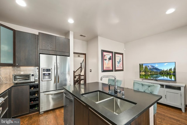 8861 Ashgrove House Ln, Vienna, VA 22182 - kitchen with appliances with stainless steel finishes, a sink, dark countertops, dark wood finished floors, and an island with sink