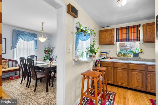 5409 20th Ave, Hyattsville, MD 20782 - kitchen featuring light countertops, light wood-style flooring, brown cabinets, crown molding, and hanging light fixtures