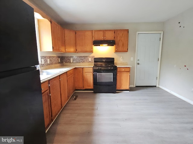 239 Grove St, Bridgeton, NJ 08302 - kitchen with black appliances, under cabinet range hood, light countertops, light wood-type flooring, and tasteful backsplash