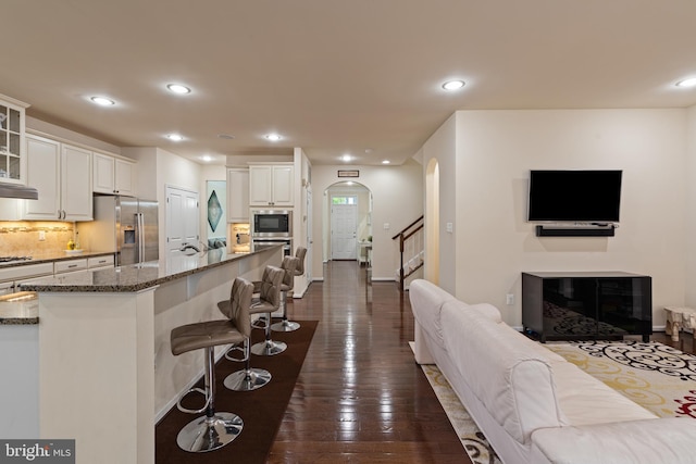 3750 Christopher Day Rd, Doylestown, PA 18902 - kitchen with appliances with stainless steel finishes, a breakfast bar, dark stone counters, arched walkways, and glass insert cabinets