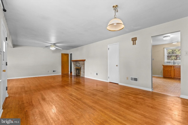 3415 E Market St, York, PA 17402 - unfurnished living room featuring ceiling fan, light wood-style flooring, a stone fireplace, and baseboards