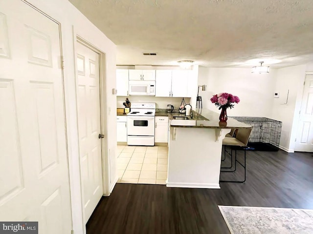 13533 Demetrias Way, Germantown, MD 20874 - kitchen featuring white appliances, a peninsula, dark countertops, white cabinets, and a breakfast bar area