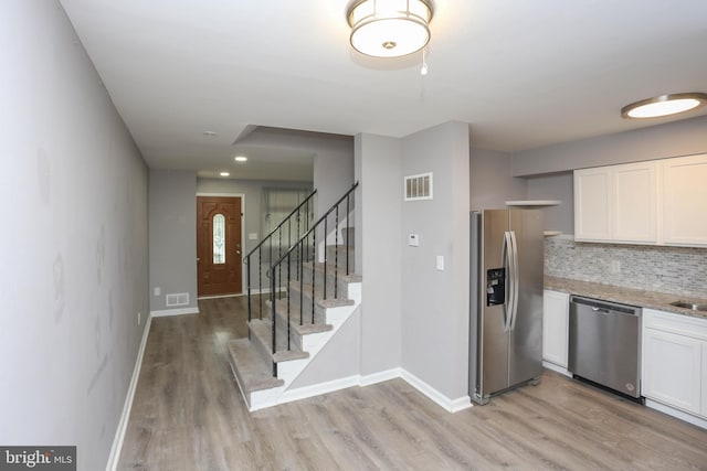 1932 Inverton Rd, Baltimore, MD 21222 - kitchen with appliances with stainless steel finishes, light wood finished floors, white cabinets, decorative backsplash, and light stone countertops