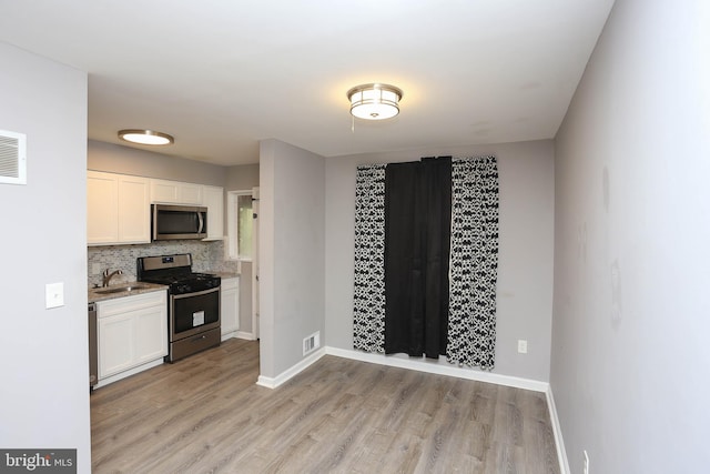 1932 Inverton Rd, Baltimore, MD 21222 - kitchen with stainless steel appliances, white cabinetry, light wood finished floors, and backsplash