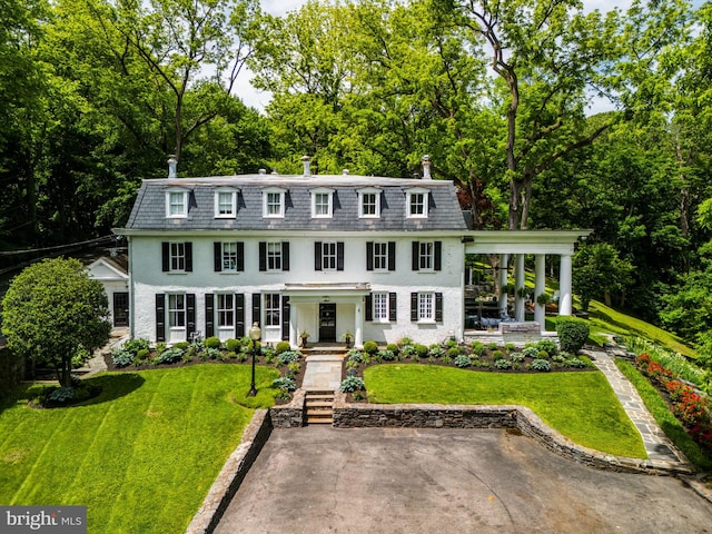 11 Conshohocken State Rd, Gladwyne, PA 19035 - view of front of house with mansard roof, covered porch, a front yard, stucco siding, and view of wooded area