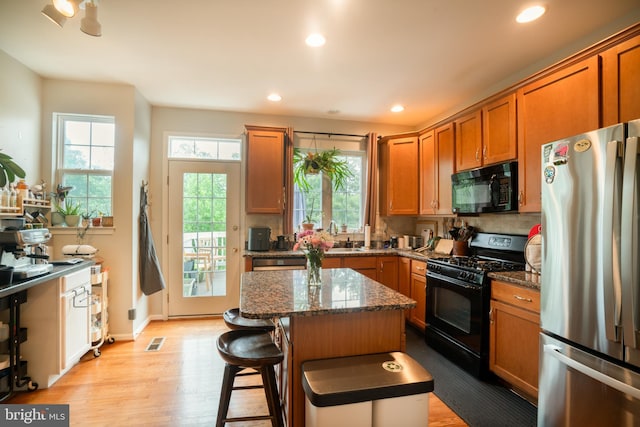20468 Alicent Ter, Ashburn, VA 20147 - kitchen with black appliances, light wood-type flooring, brown cabinetry, a center island, and dark stone countertops
