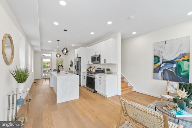 713 Tewkesbury Pl NW, Washington, DC 20012 - kitchen featuring appliances with stainless steel finishes, a sink, white cabinets, an island with sink, and light wood-style flooring