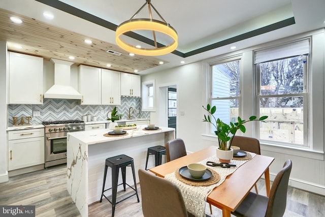 837 W 33rd St, Baltimore, MD 21211 - kitchen with stainless steel range, custom exhaust hood, backsplash, light wood-style flooring, and white cabinets