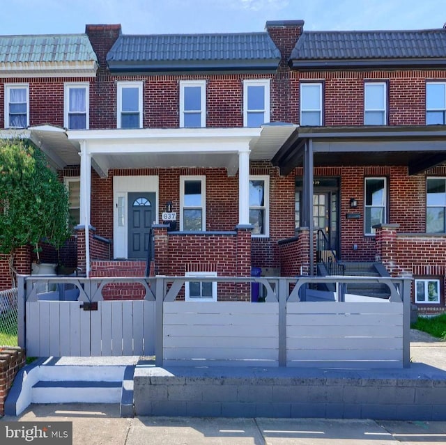 837 W 33rd St, Baltimore, MD 21211 - townhome / multi-family property with brick siding, a fenced front yard, covered porch, and a tiled roof