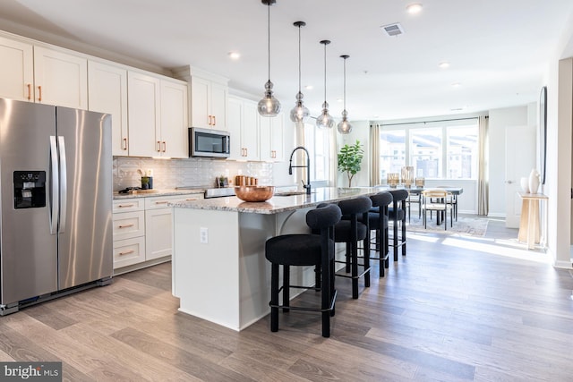 10009B American Pharoah Ln, Laurel, MD 20723 - kitchen featuring appliances with stainless steel finishes, a sink, a kitchen island with sink, light wood-style floors, and backsplash