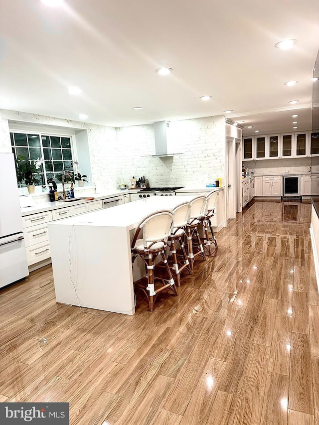 1319 Remington Rd, Wynnewood, PA 19096 - kitchen with beverage cooler, wall chimney range hood, decorative backsplash, light wood-type flooring, and light countertops