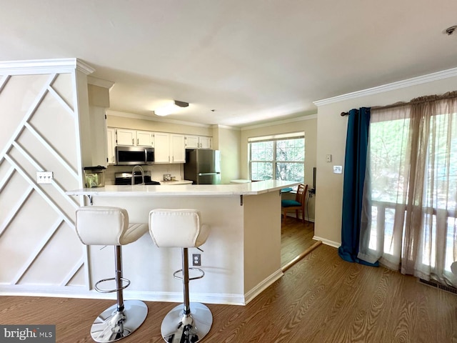 6820 Jade Ct, Capitol Heights, MD 20743 - kitchen featuring appliances with stainless steel finishes, dark wood-type flooring, a peninsula, a breakfast bar area, and ornamental molding