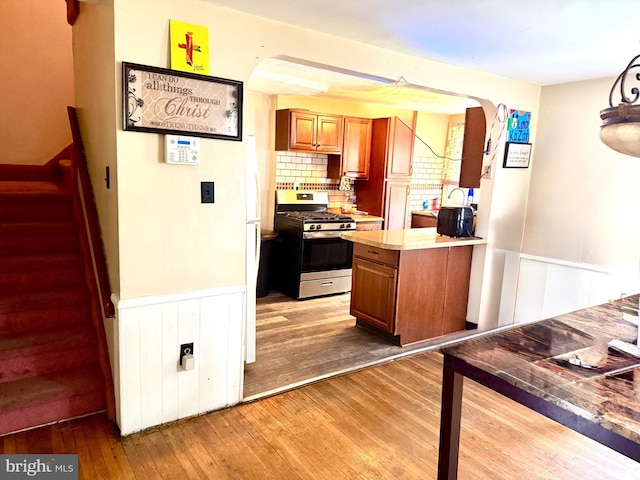 3141 S Atlanta Rd, Camden, NJ 08104 - kitchen featuring stainless steel range with gas stovetop, brown cabinetry, hardwood / wood-style floors, wainscoting, and arched walkways