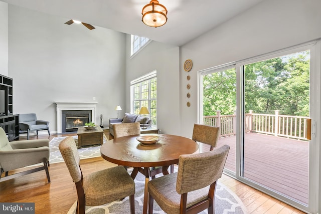 17542 Falls Pl, Round Hill, VA 20141 - dining space with light wood-style flooring, a glass covered fireplace, a ceiling fan, and a towering ceiling