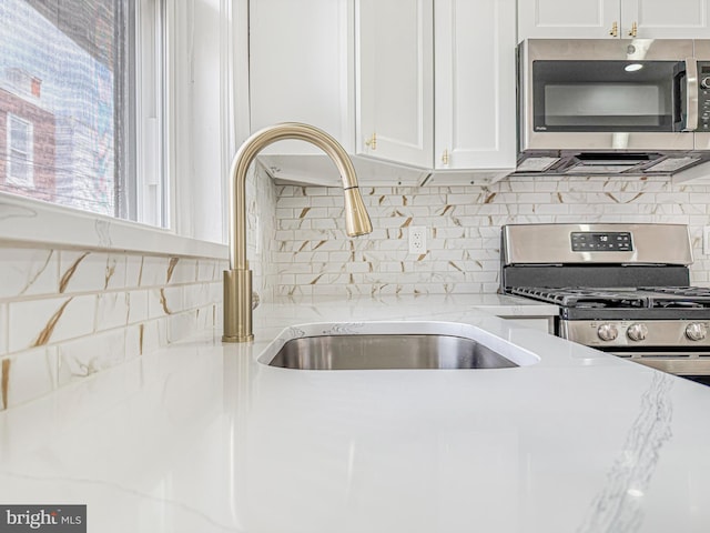 5849 Washington Ave, Philadelphia, PA 19143 - kitchen featuring appliances with stainless steel finishes, white cabinetry, a sink, light stone counters, and backsplash