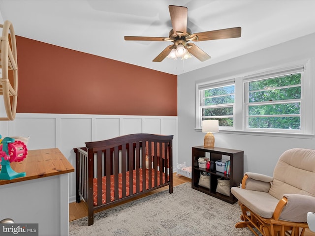 303 Stevens Ave, Reading, PA 19608 - bedroom featuring a nursery area, wainscoting, wood finished floors, and a ceiling fan