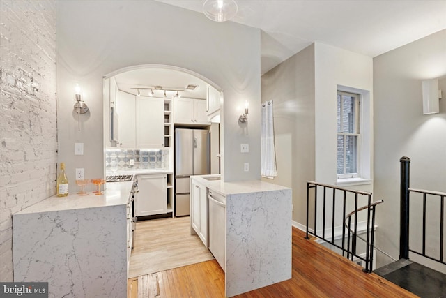 1017 Spruce St Unit C, Philadelphia, PA 19107 - kitchen with arched walkways, light wood-style flooring, stainless steel appliances, white cabinets, and tasteful backsplash