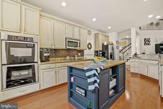 11742 Maid At Arms Ln, Berlin, MD 21811 - kitchen with stainless steel appliances, open shelves, light wood-type flooring, cream cabinets, and decorative backsplash